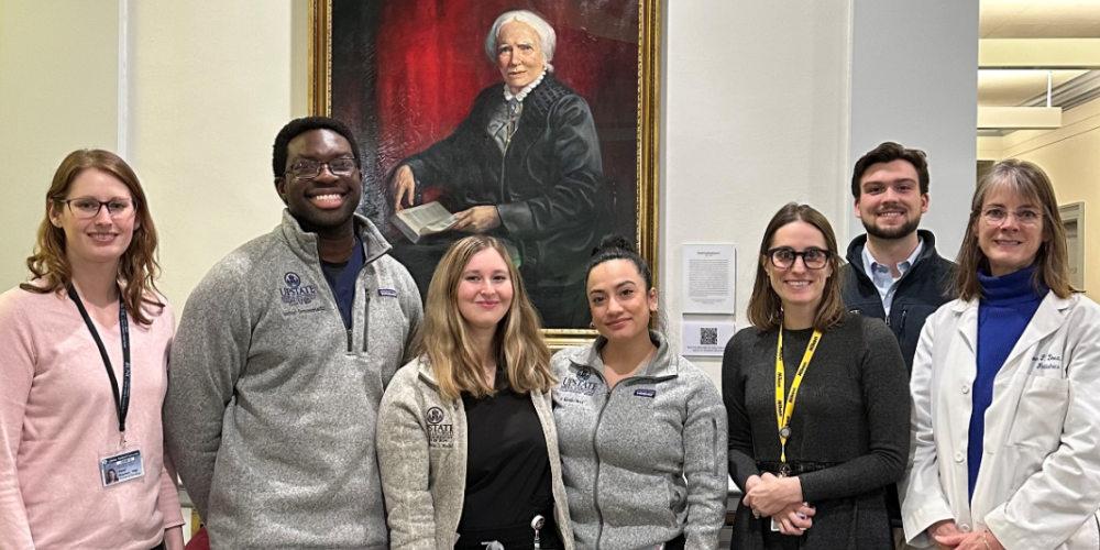 Happy students and faculty in front of a portrait of Elizabeth Blackwell