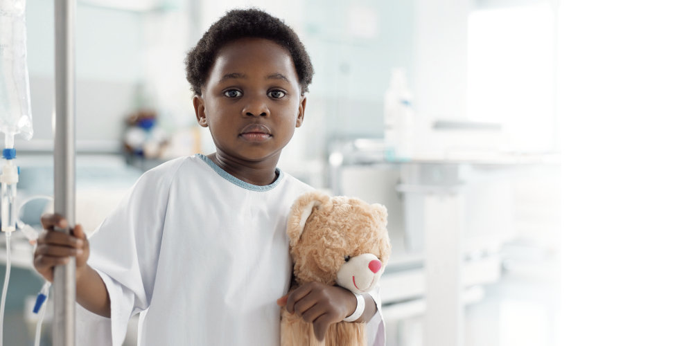 Pediatric patient holding IV pole and teddy bear looking straight ahead
