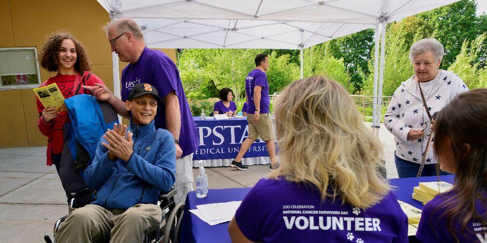Volunteers are assisting a cancer patient at a registration table at the National Cancer Survivors Day celebration at the Rosamond Gifford Zoo.