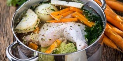Stainless steel pot filled with chicken leg, carrots, onions and fresh herbs and water.