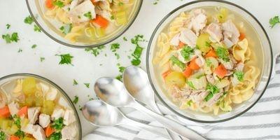 3 glass bowls filled with chicken broth, egg noodles, bite-sized pieces of chicken, carrots and celery garnished with fresh parsley.