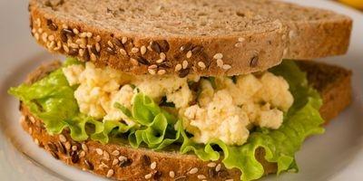Homemade egg salad with leafy green lettuce between two slices of multi-grain bread.