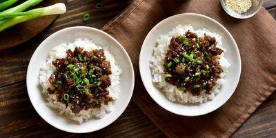 Two white bowls filled with white rice and topped with ground beef garnished with green onions and sesame seeds.