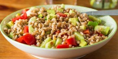 White bowl filled with farro, chunks of cucumber and tomato.