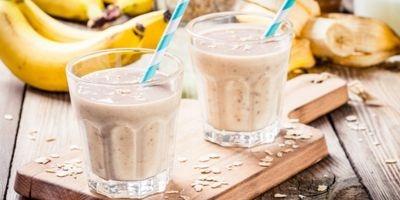 Two glasses filled with peanut butter banana smoothie with a white and blue striped straw.