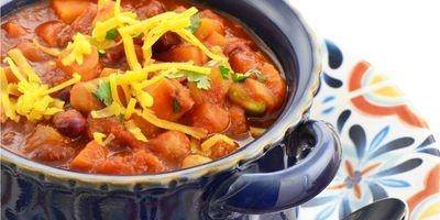 Blue crock filled with vegetarian chili garnished with shredded cheddar cheese.