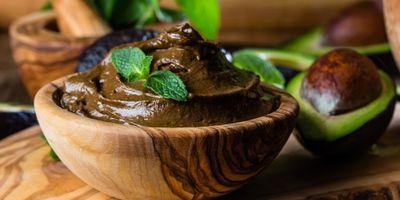 Wooden bowl filled with avocado chocolate mousse garnished with a mint leaf.