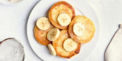 Four cottage cheese pancakes on a white plate garnished with banana slices and powdered sugar,