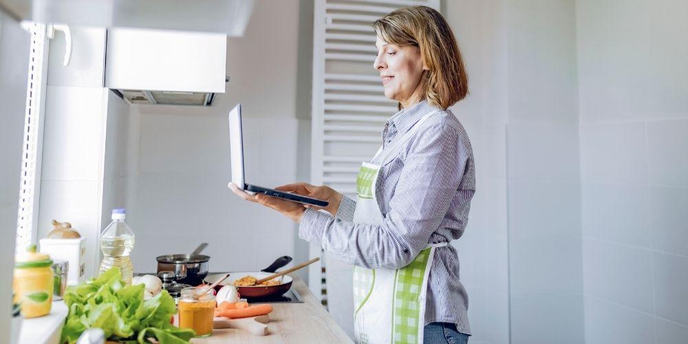 Woman wearing an apron following a recipe on her laptop computer.