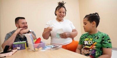 A student or technician teaching a child how to label pictures of items with a case manager observing
