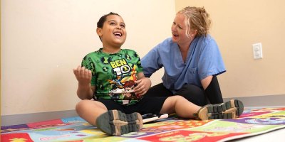 A student or technician sitting on the ground with a child while laughing and interacting