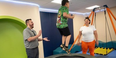 A student or technician and case manager smiling as a child jumps on a trampoline
