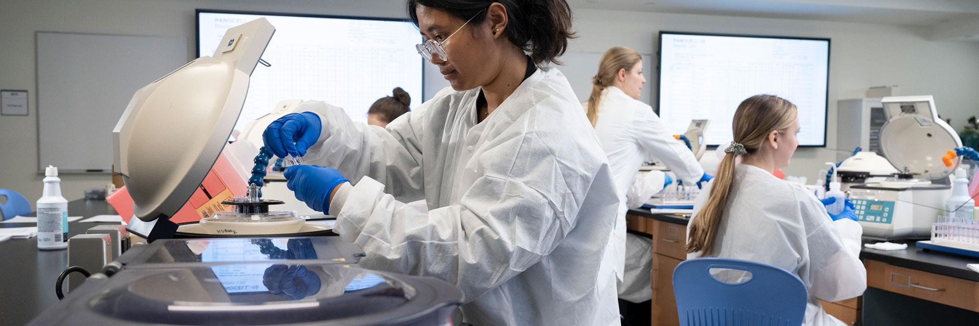 Medical Students learning within the classroom, with one removing samples from a centrifuge