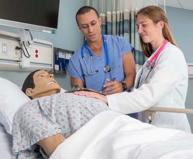 Nurses Michael Ortiz, left, and Taryn Bitzer practice their skills on a high-tech dummy that can produce the reactions and medical problems of a real patient in the Simulation Center at Upstate Medical University. Ortiz works at Upstate University Hospital, and Bitzer works at Crouse Hospital; both are studying to be nurse practitioners at the Upstate College of Nursing. (photo by Robert Mescavage)