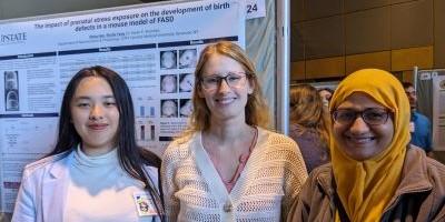 Three women standing in front of a scientific poster.