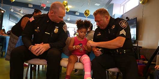 Onondaga County Sheriff's Office Lieutenant Christopher Koeppe and Sergeant Jon Seeber present Sarai, an Upstate Golisano Children's Hospital patient, an official sheriff's badge at the second-annual Onondaga County Sheriff's Pizza Party