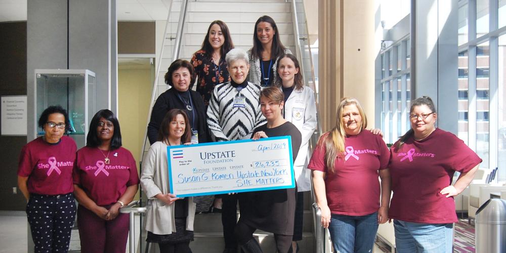 She Matters Resident Health Advocates and Upstate staff accept a check from the Susan G. Komen of Upstate New York organization in the lobby of the Upstate Cancer Center.