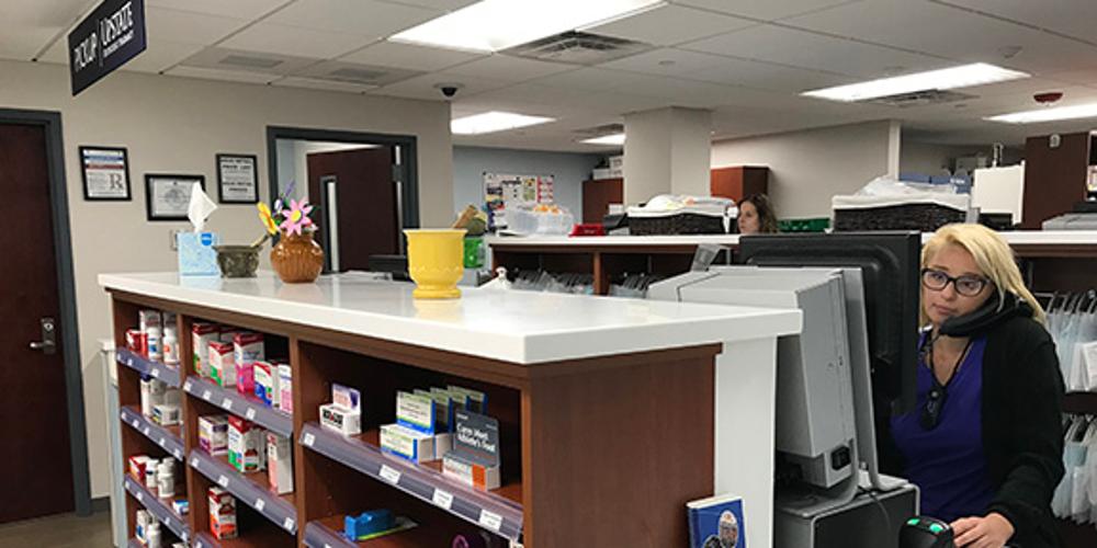 A pharmacist sits behind a computer while on the phone inside Upstate's Outpatient Pharmacy.