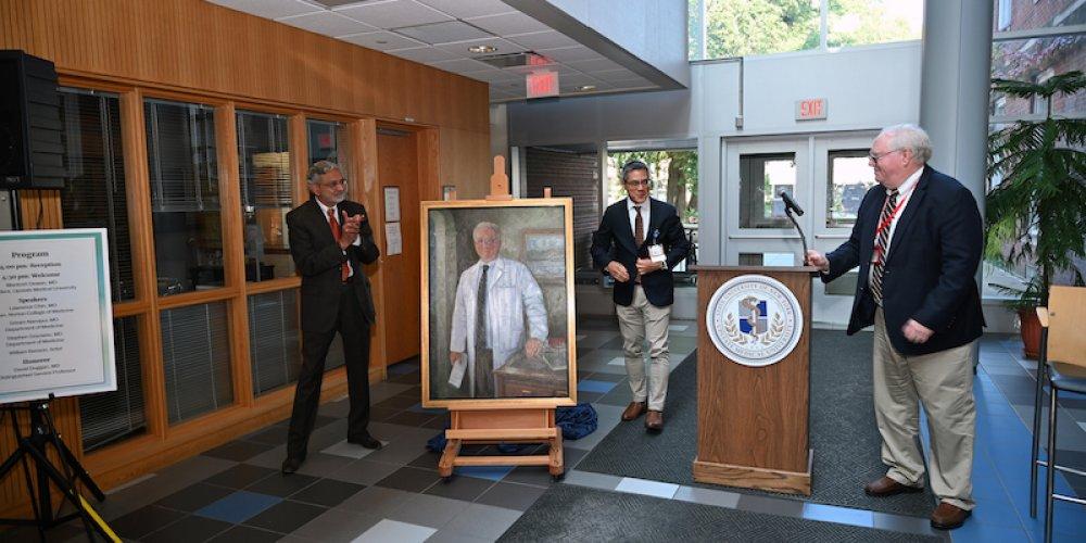 PORTRAIT UNVEILED: Dr. David Duggan, MD, right, looks on as Upstate President Dr. Mantosh Dewan, left, and Norton College of Medicine Dean Dr. Lawrence Chin unveil a portrait of Duggan during a reception Aug. 28. Duggan’s selection to the Upstate Portrait Gallery acknowledges his more than four decades of service to Upstate, beginning with his enrollment in medical school. Duggan has held many positions over the years, including dean of the College of Medicine, chair of the Department of Medicine and medical director of Upstate University Hospital. Portrait painter is William Benson.