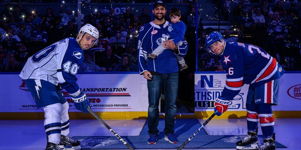 FACE OFF:  Joe Batista, RN, an adult hematology oncology nurse with the Upstate Cancer Center, is at center ice for the ceremonial puck drop for the Syracuse Crunch “Shine a Light” on lung cancer night Nov. 4 at Upstate Medical University Arena. Batista was aided on the puck drop by his 2 year-old son, Anthony.