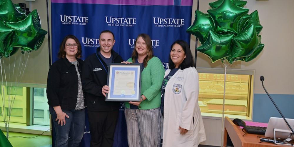 INJURY PREVENTION OUTREACH: Syracuse Corporation Counsel Susan Katzoff, left, presents a proclamation from the City of Syracuse declaring Nov. 18 as Upstate Goes Green for Injury Prevention Day. Joining Katzoff at the presentation are, from left, Anthony Scalise, BSN, RN, trauma injury prevention; Elizabeth Sapio, Safe Kids Upstate New York coordinator; and Roseanna Guzman-Curtis, MD, MPH, Upstate Trauma Center medical director. Several buildings in the Syracuse area were illuminated in green to mark Injury Prevention Day, including JMA Wireless Dome, Weiskotten Hall and Syracuse City Hall, among others.