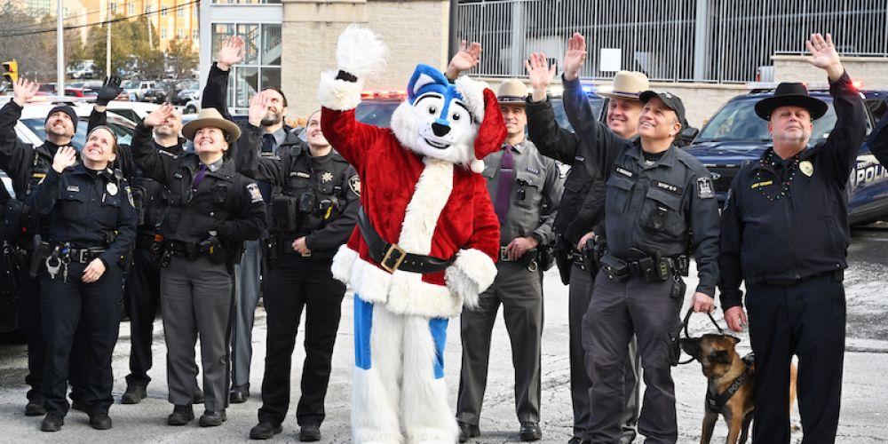 GREETINGS FOR THE KIDS: Officers from more than a dozen law enforcement and first responder agencies, along with Upstate University Police and Upstate’s mascot, Hero, gather Dec. 22 outside Upstate Golisano Children’s Hospital to send holiday wishes to the children, who watched from a top floor of the hospital. The officers arrived in motorcade of emergency vehicles with flashing lights and sirens.