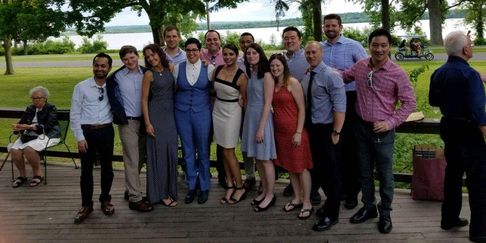 Image of a diverse group of young adults, dressed for a summer cocktail party, posing for a group photo on an outdoor deck