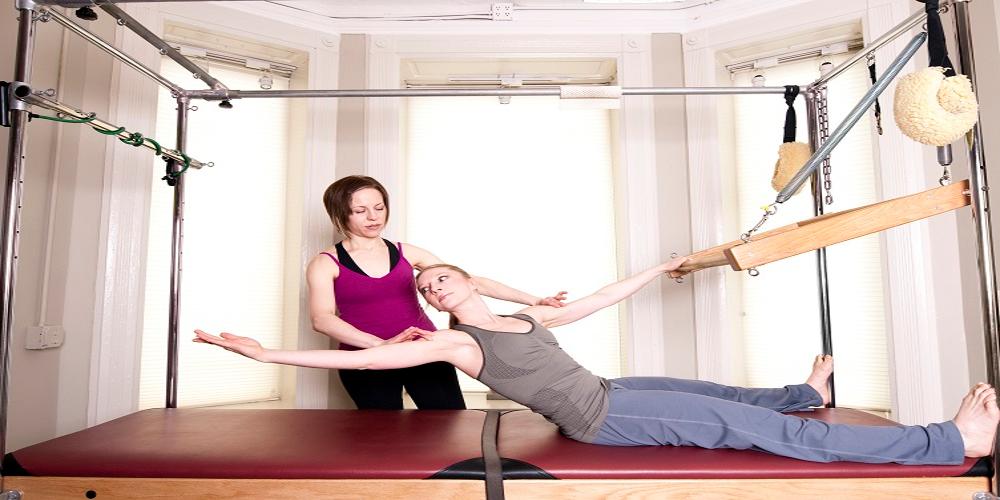 Therapist assisting patient through use of pilates machine and stretching backwards.