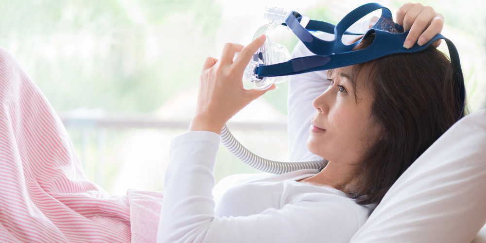 Woman in bed putting her cpap mask on