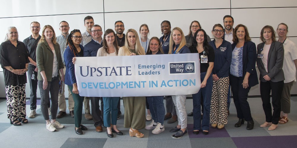 A large group of emerging leaders pose in front of a sign for the program with the words Development in Action