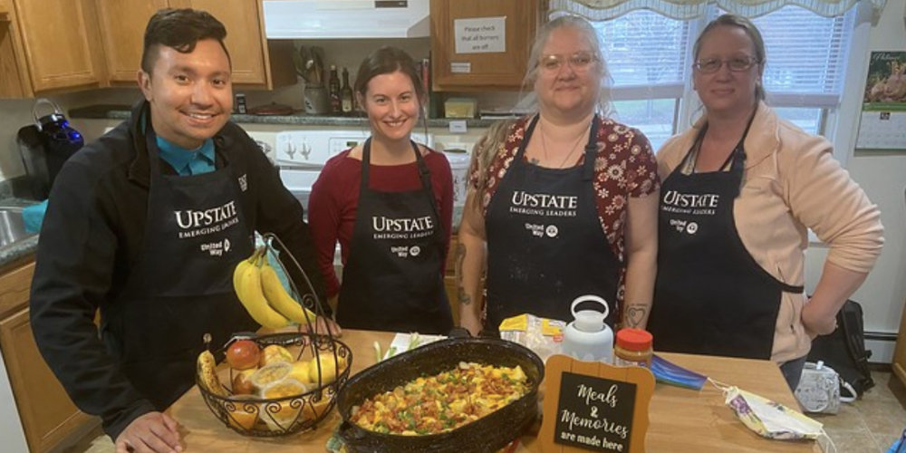 Five emerging leaders smile while preparing food at Sarah's Guest House