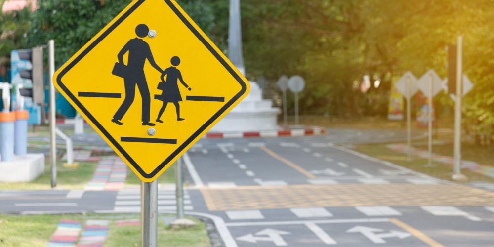 Image of an empty crosswalk with a traffic sign showing pedestrians on a sunny morning