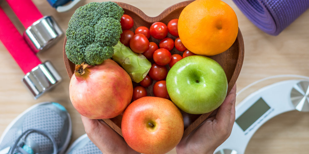 Fruit and vegetables in a heart-shaped bowl and exersise equipment around it