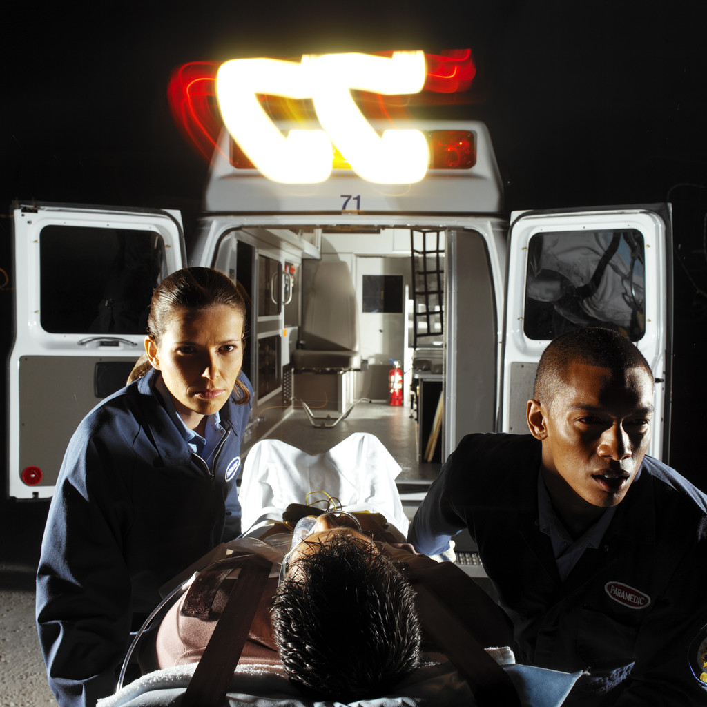 Two Young Paramedics Wheeling a Male Patient on a Stretcher Out of An Ambulance Two Young Paramedics Wheeling a Male Patient on a Stretcher Out of An Ambulance