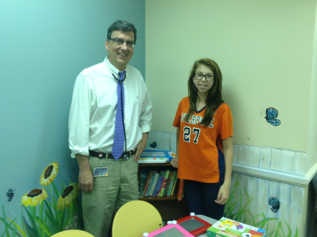 Girl Scout Nicole Abbott stands with her doctor, Dr. William Hannan, MD in front of the bookshelf she donated.