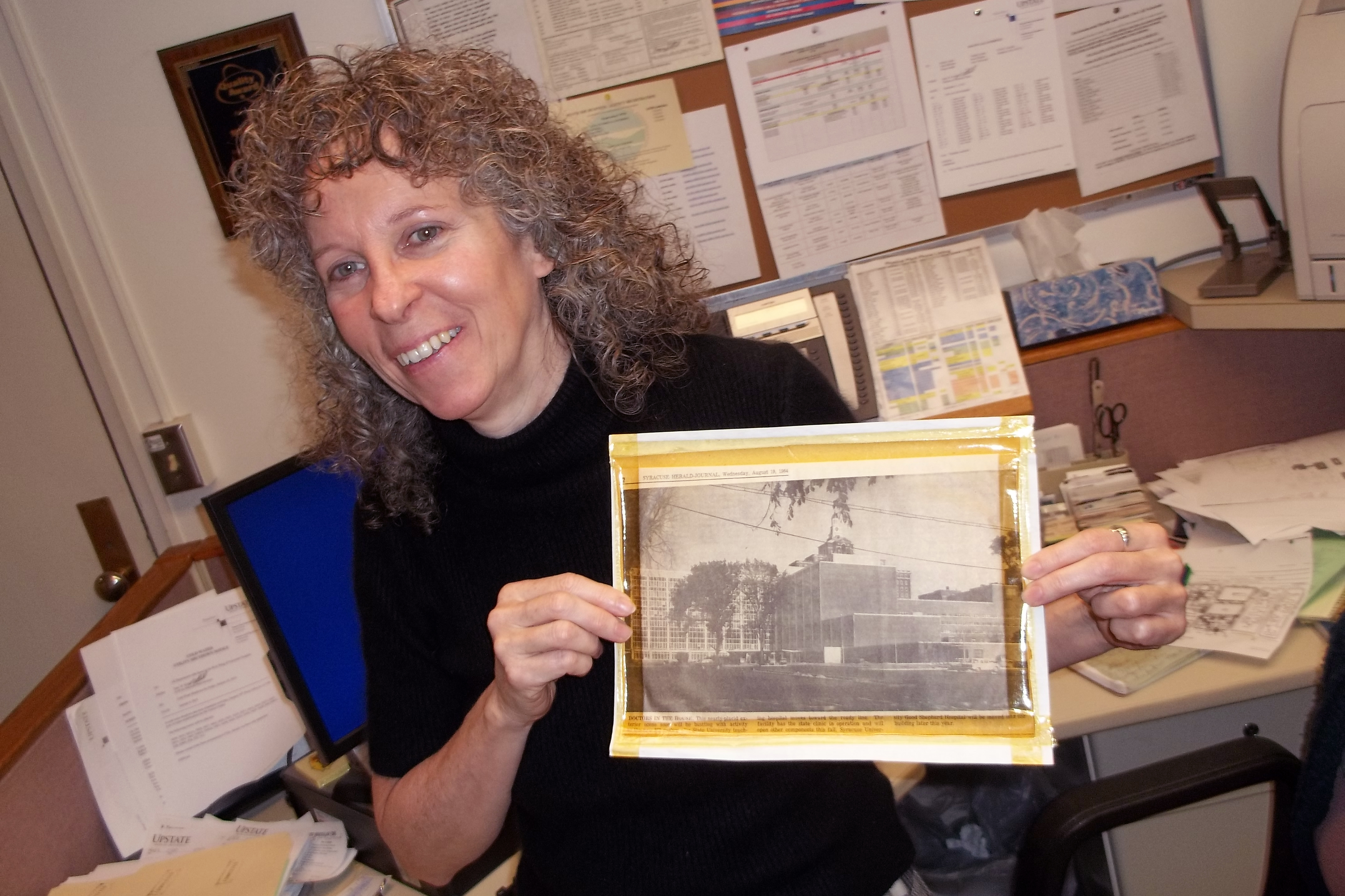Mary Lent holds a 50-year-old news clipping showing construction of the hospital at Upstate‘s downtown Syracuse campus.