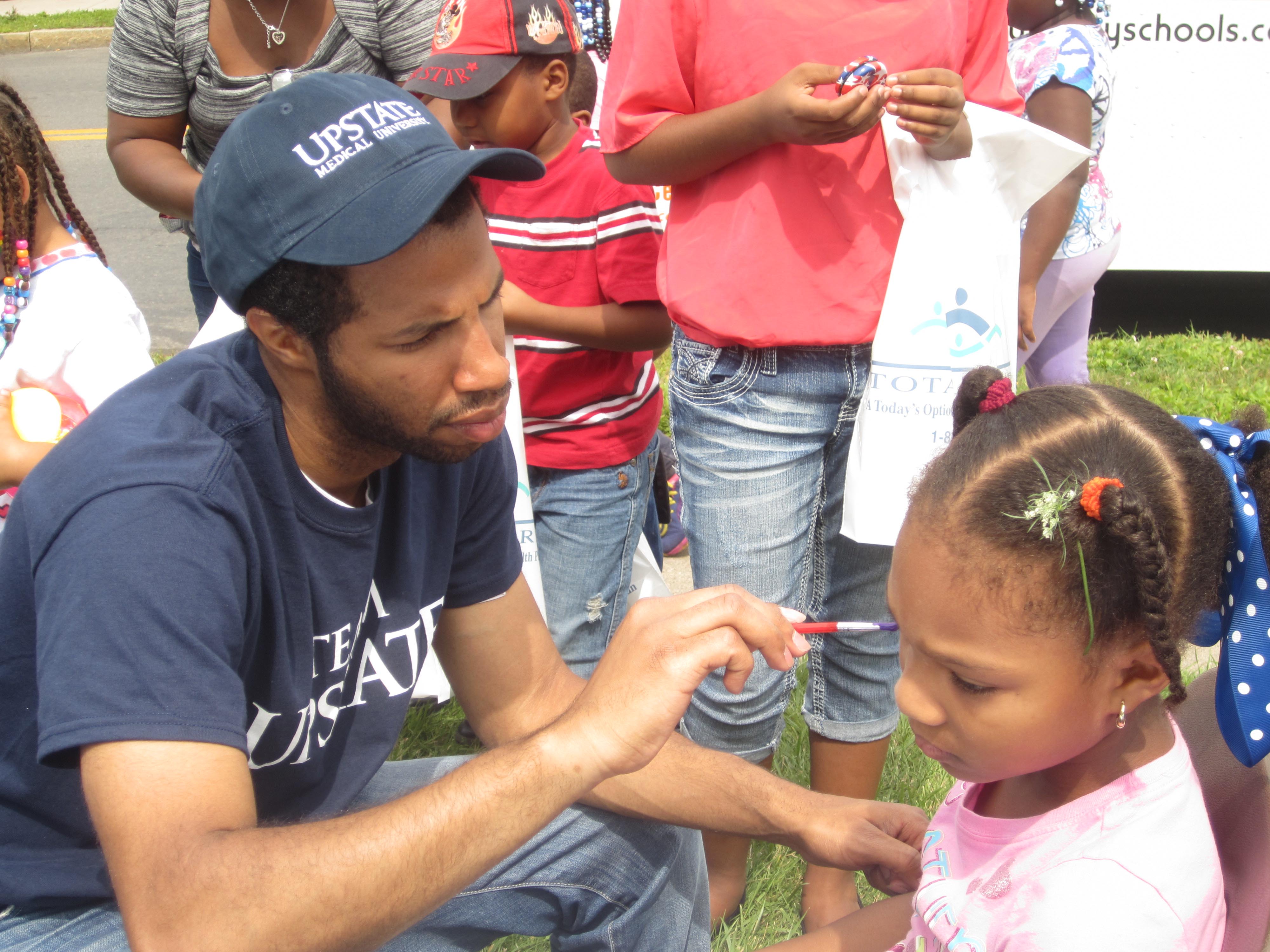Medical student Alex Rodriguez paints the face of a young student at the Back To School Barbeque.