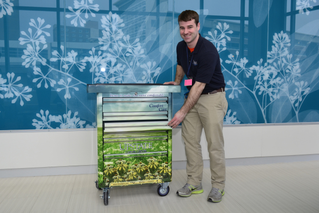 Brandon Spillett, of Syracuse, an Upstate volunteer, shows the Comfort Cart, which offers items to patients at the Upstate Cancer Center. (PHOTO BY DEBBIE REXINE)