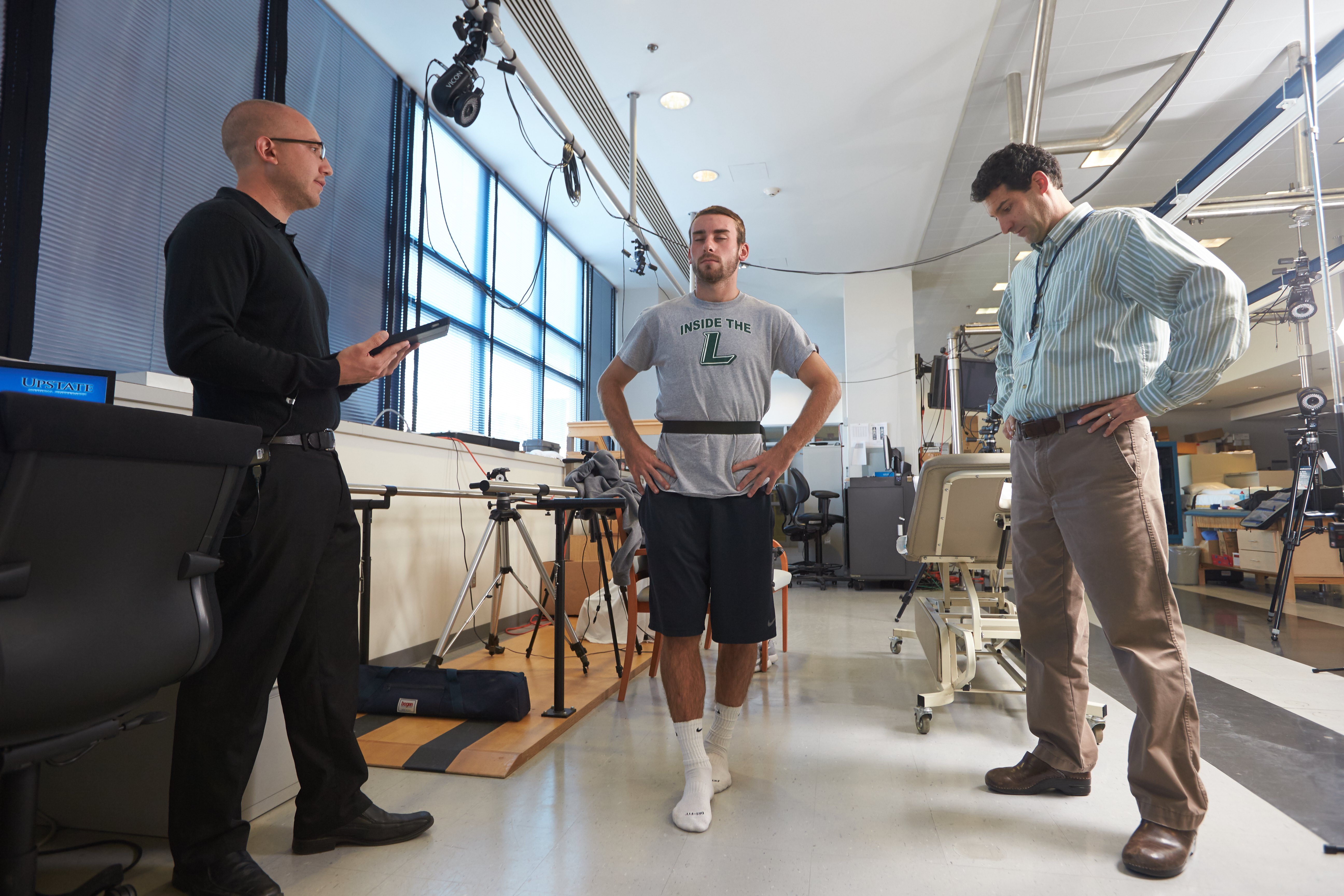 Slack, center, stands on a straight line with his eyes closed to test his physical functions, watched by athletic trainer Joshua Baracks (left) and project director Christopher Neville, PhD. Before that, test subjects are asked to recite a series of words and count backwards, and afterward, an EEG is used to track and record brain patterns.