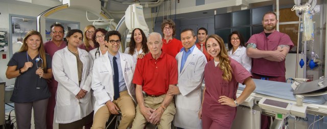 Larry Deshaw, 78, (center in red) survived what could have been a fatal stroke because of multiple crucial decisions that were made quickly, including: 1. Wife, Nancy Humphrey (behind him) recognized the signs of a stroke and immediately called 911. 2. Rescuers in Clayton made the decision to send Deshaw directly to the comprehensive stroke center at Upstate University Hospital by helicopter so he would arrive as quickly as possible. 3. Stroke specialists at Upstate led by Gene Latorre, MD, (to the right of Deshaw) established a protocol that directs every patient suspected of having a stroke straight to the computerized tomography suite in the emergency department on arrival. The prompt CT scan reveals whether it's safe to give the patient clot-busting medication. A rapid CT angiogram was then used to identify the blocked artery and plan interventional treatment. 4. The hospital is outfitted with a modern interventional radiology suite that is available around the clock and staffed by doctors including Hesham Masoud, MD, (to the left of Deshaw) who have expertise in endovascular surgical neuroradiology - which means they are skilled at swiftly retrieving blood clots from the brain.