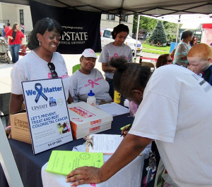 Janet Bacon (left) and Martha Chavis-Bonner (seated), both of whom are resident health advocates, sign people up for mammograms and colorectal cancer screening at the Mary Nelson Back to School Barbecue, held in August in Syracuse. (PHOTO BY SUSAN KEETER)
