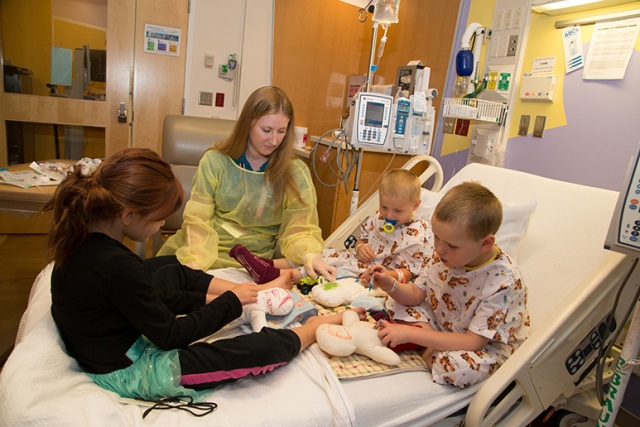 Maggie Zick, a certified child life specialist at Upstate Golisano Children's Hospital, leads the Delaney brothers, Trevor and Michel, and their sister Elizabeth in medical play at the bedside. Medical play is a tool that child life specialists use to explain procedures to patients and that offers a way to include siblings, who may feel left out. This photo was selected for the 2017-2018 Children's Hospital Association's traveling photo exhibition, which promotes the value of children's hospitals nationwide. (PHOTO BY KATHLEEN PAICE FROIO)