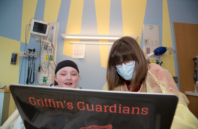 Fazzini, in mask, helps Hailey work on a photo she took. Hailey enjoys all types of art but especially photography. They are altering the photo using Photoshop software, which, along with the laptop, was donated by the charitable group Griffin's Guardians.