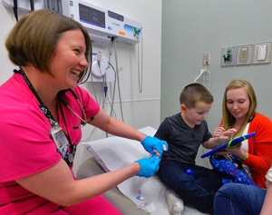 At a checkup session in May, nurse Yvonne Dolce pricks Greyson's fingers to get a blood sample while he is absorbed in an electronic game, thanks to child life specialist Sarah Buck, right.