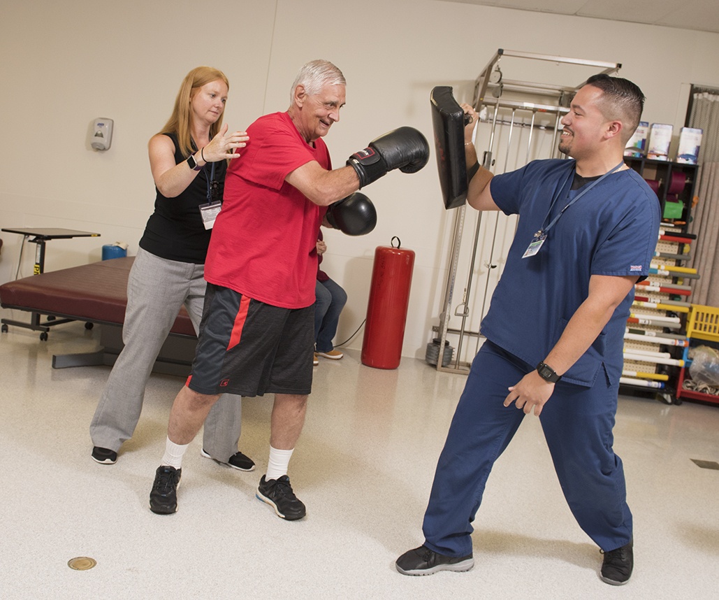 Physical therapist Kelly Grier, left, tailored a recovery program for William Bouchard, an avid martial artist, that included boxing. Physical medicine and rehabilitation student Joey Feliciano assisted by holding targets for Bouchard. (PHOTO BY SUSAN KAHN)
