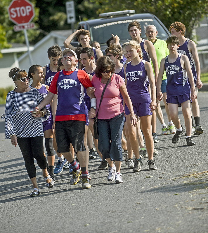 William Doney, center, celebrates his 84th birthday by walking through Watertown with community members and the Watertown High School cross-country teams. (PHOTO BY AMANDA MORRISON/ WATERTOWN DAILY TIMES)