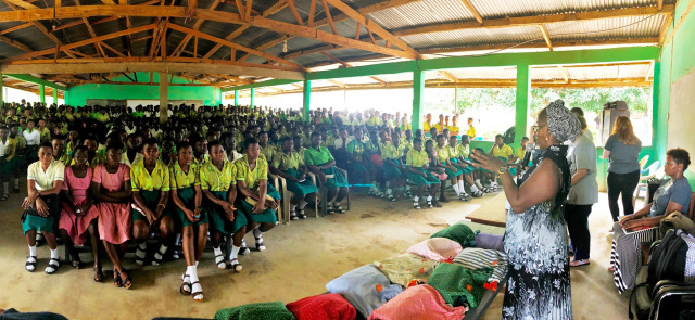 Nearly 1,000 girls assembled in an open-air classroom at Namong Senior High School in Offinso, Ghana, to receive menstrual education from a team of ASAP volunteers. Students with the greatest need received reusable menstrual kits made by the nonprofit organization Days for Girls. At right in the blue flowered dress is Nancy Addo, headmistress of the school. At far right, seated, is Upstate nurse Maisha Brown, a volunteer for ASAP, which stands for the Americans Serving Abroad Program. (PHOTO BY MEGAN LEWIS)