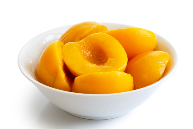 Canned peach halves in bowl isolated on white background.