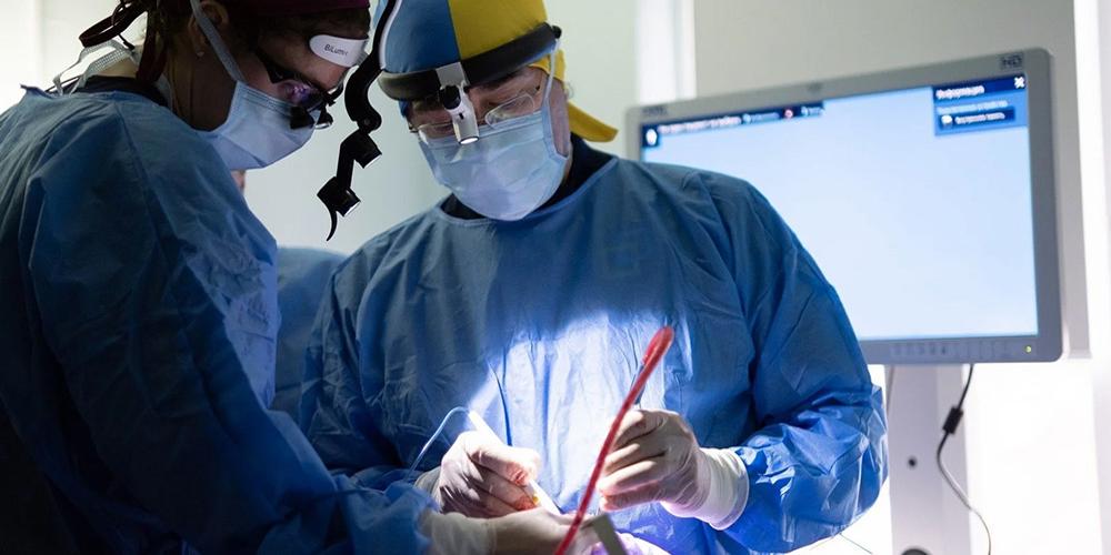 Upstate's Sherard Tatum, MD (right), was among a team of facial and plastic surgeons who traveled to Ukraine to treat people with severe war wounds. His surgical hat is the color of the Ukrainian flag.