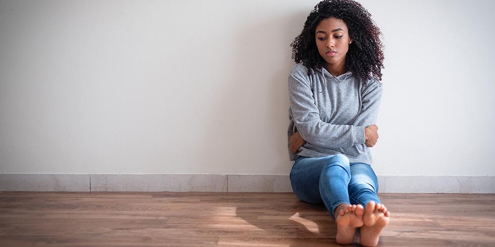 Image of a sad-looking teen girl sitting by herself on the floor of an empty room